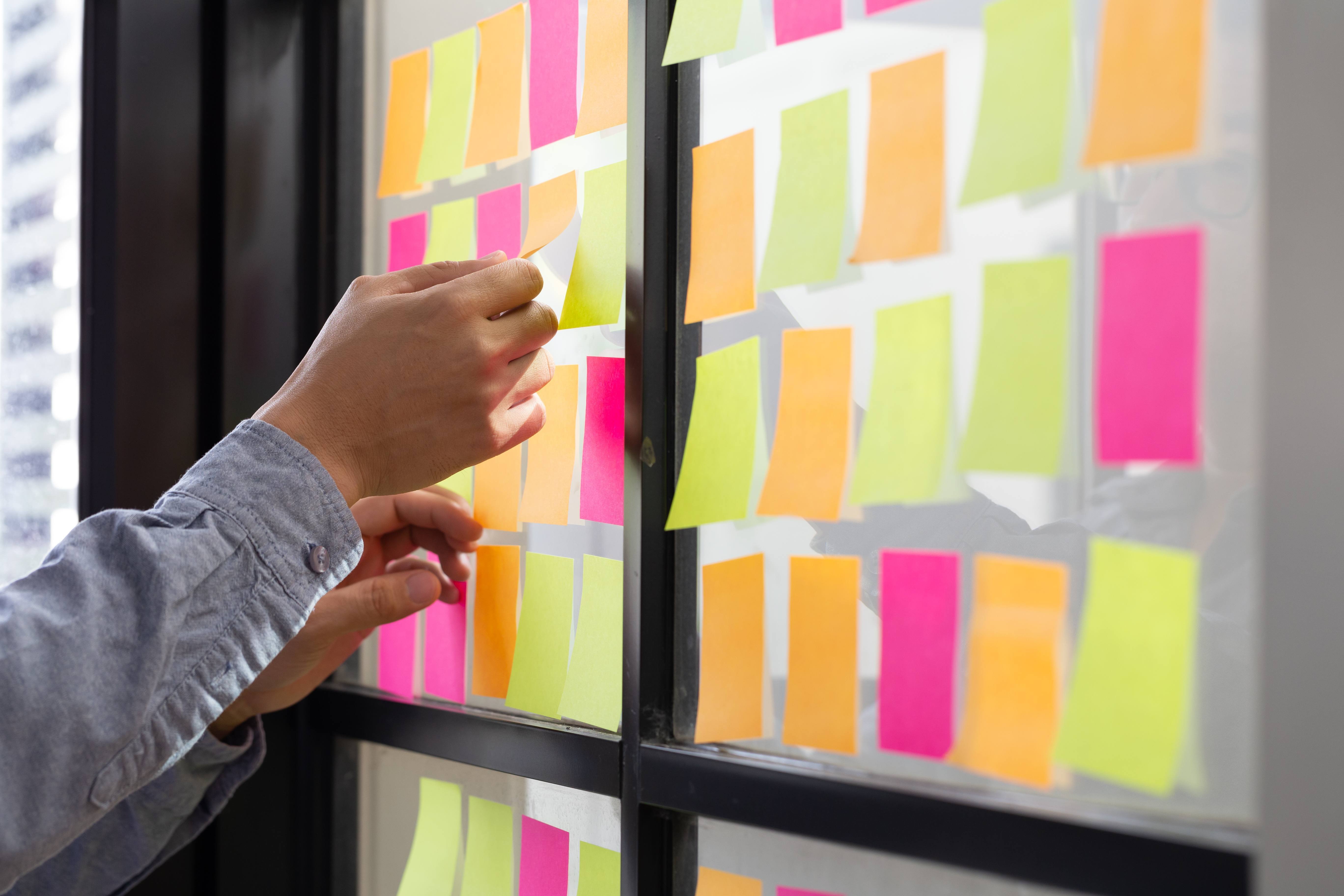 it-worker-tracking-his-tasks-kanban-board-using-task-control-agile-development-methodology-man-attaching-sticky-note-scrum-task-board-office (2)